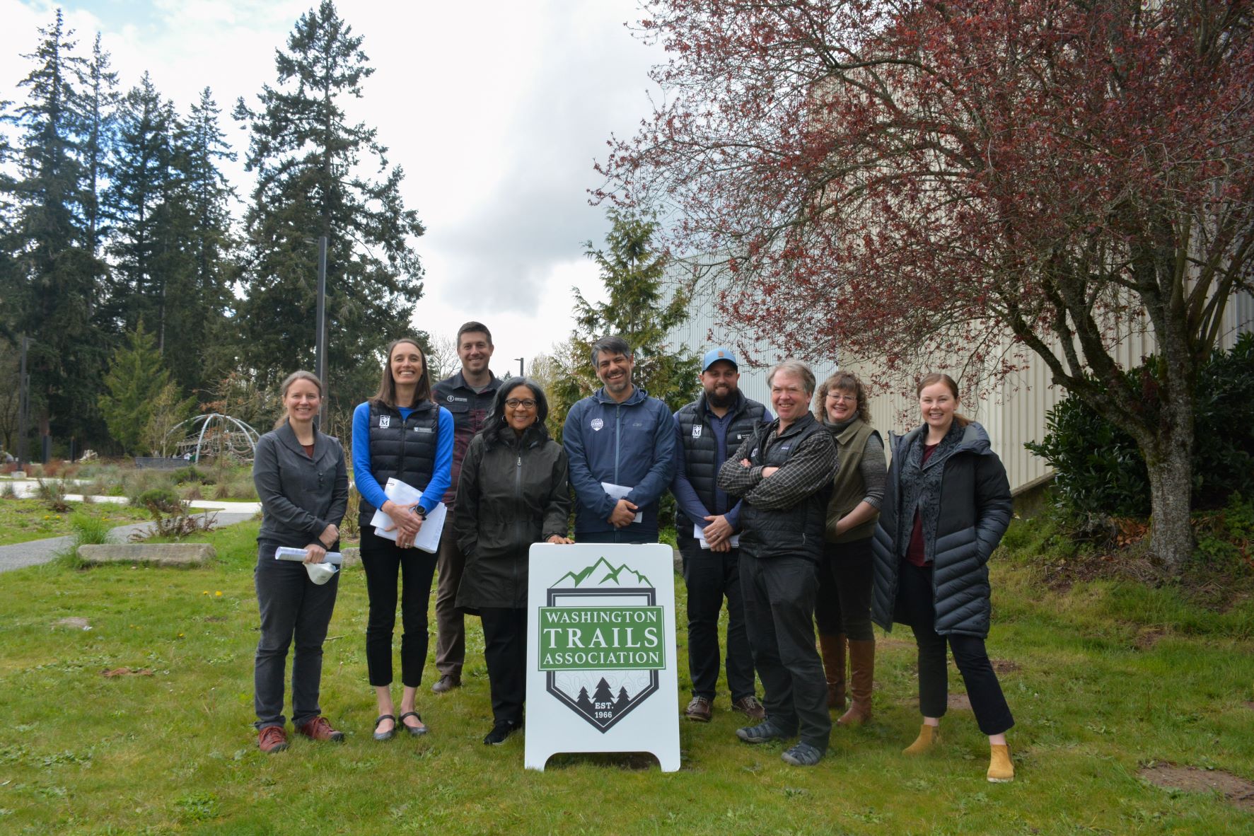 Group of people gather around Washington Trails Association sign, looking at camera.