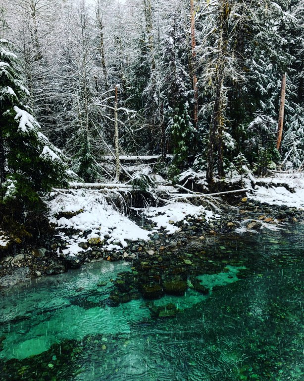 Photo by Jessica Dobervich. Snow falls on a turquoise body of water deep in the snowy mountains.
