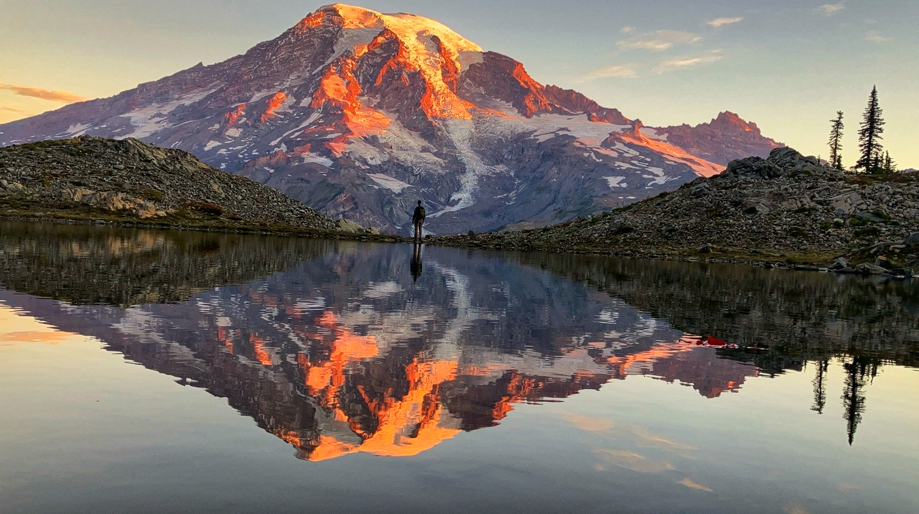 Silhouette of a hiker standing in front of Mount Rainier, reflected in a lake below