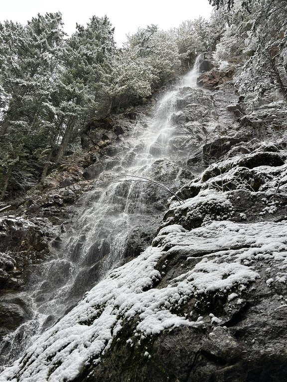 Large waterfall with water cascading down, covered in snow.