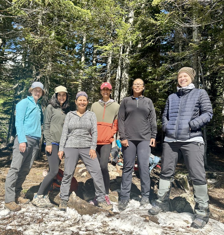 Group of 6 people stand on a trail with trees in the background