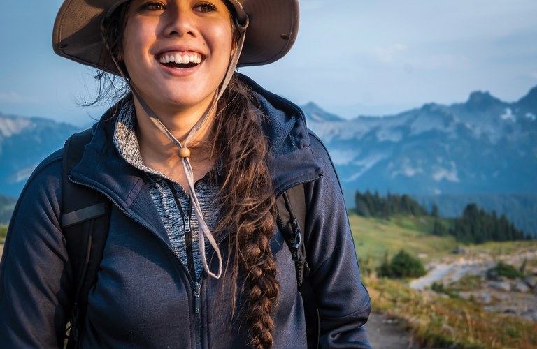 A young woman with a dark braid and sun hat smiles. 
