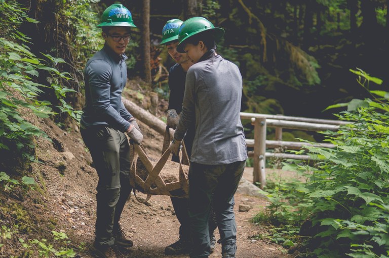 Three volunteers use a rock net to move a large rock. 