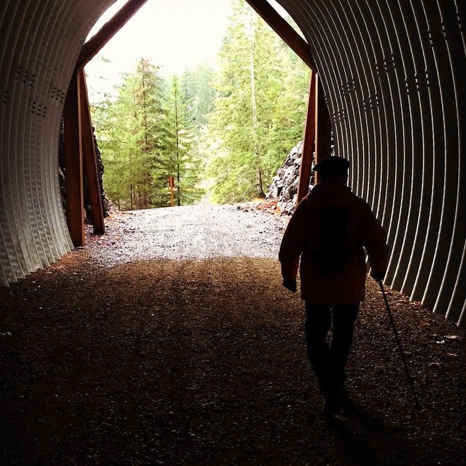 A hiker walking into the light at the end of an old railroad tunnel. Photo by maryvr. 