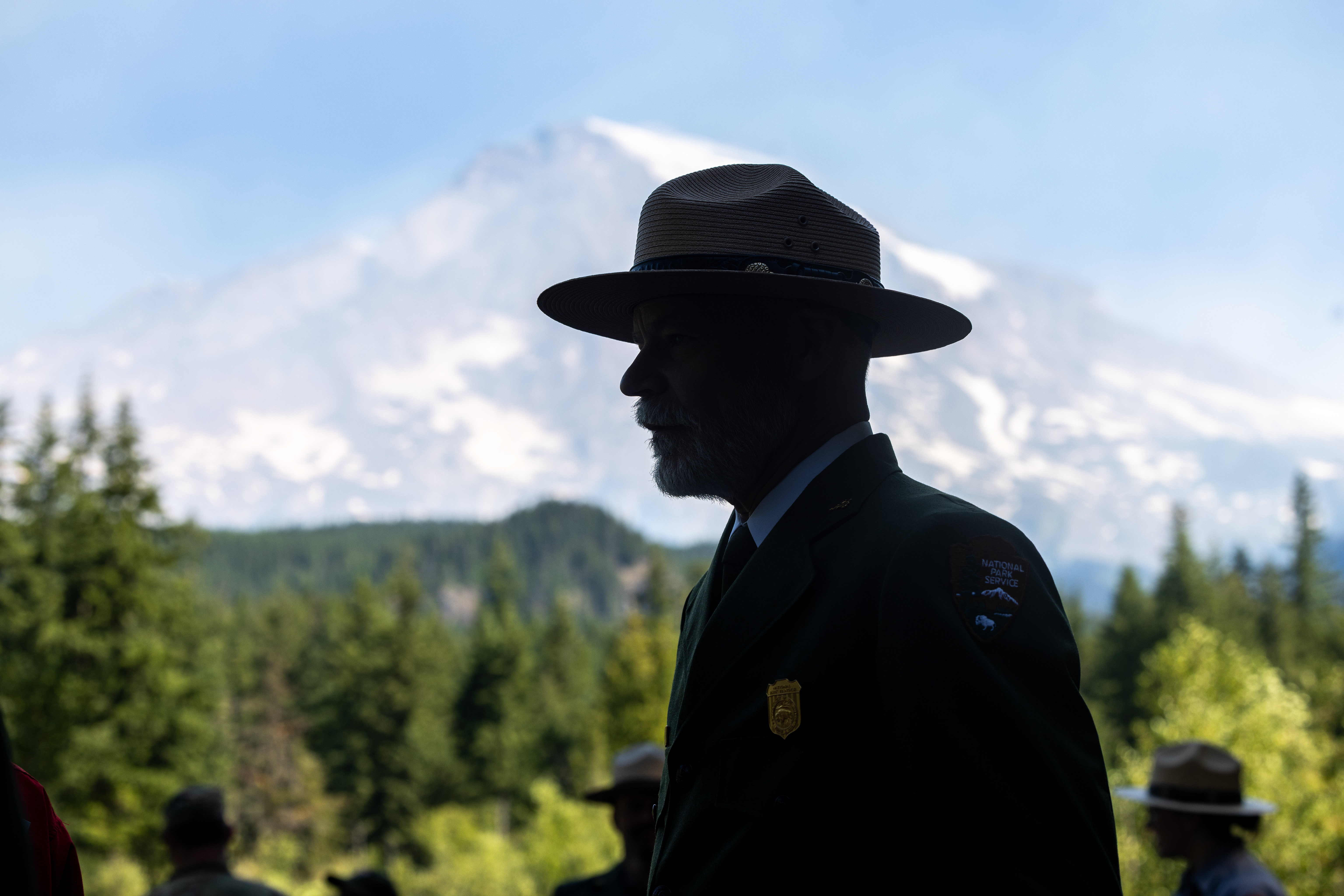 An NPS staff member in uniform silhouetted against Mount Rainier