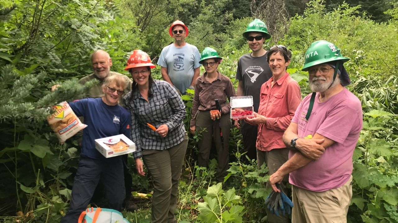 Seven people smile at camera. Holding treats on trails.