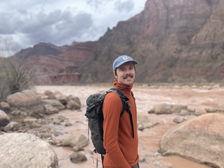 A hiker stands next to a muddy river.