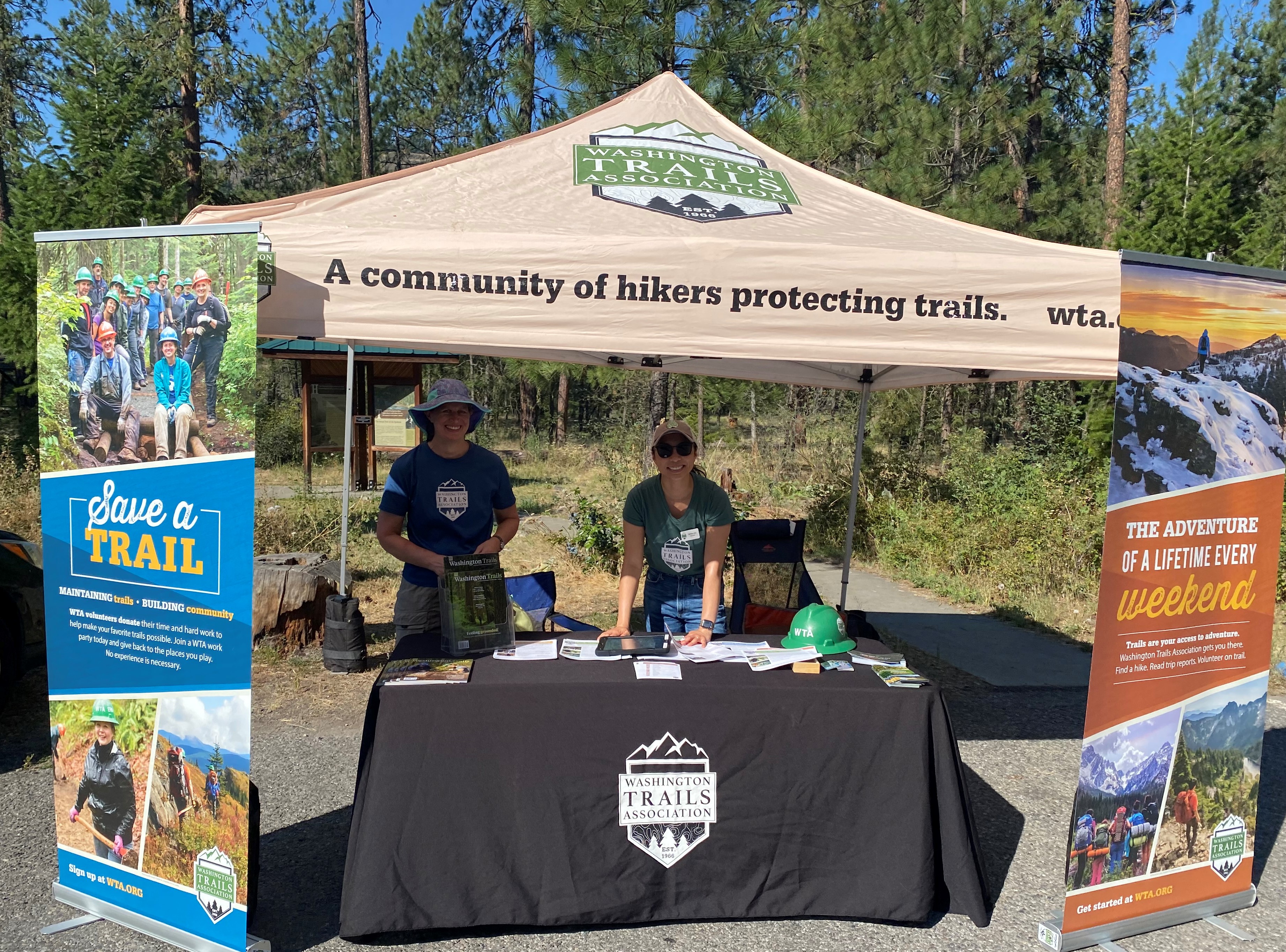 Volunteer smile underneath a WTA canopy while volunteering on Washington Trails Day.