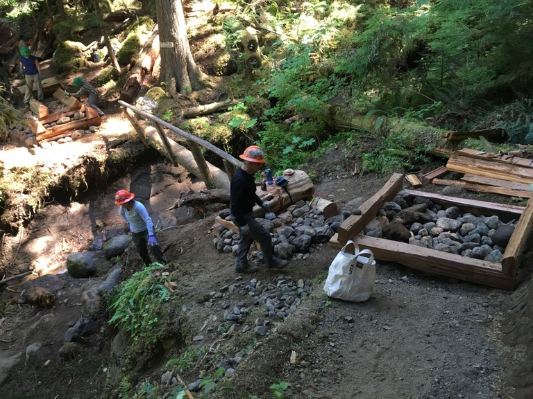 Two people work in the shade, building a footing for a bridge